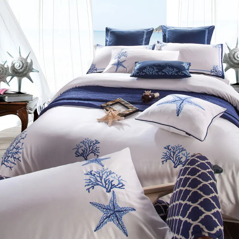 Blue coral and starfish embroidered duvet cover with navy accent pillows on a crisp white bed – L&B