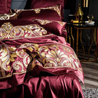Layered burgundy and gold embroidered bedding shown from an elegant bedside view, ZUTAPERA – L&B