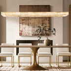 Alabaster linear chandelier above a dining table in a warm minimalist dining room with a gold canopy