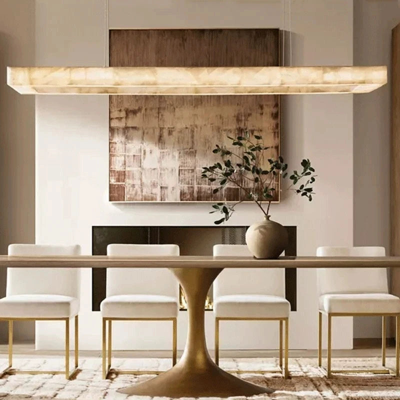 Alabaster linear chandelier above a dining table in a warm minimalist dining room with a gold canopy