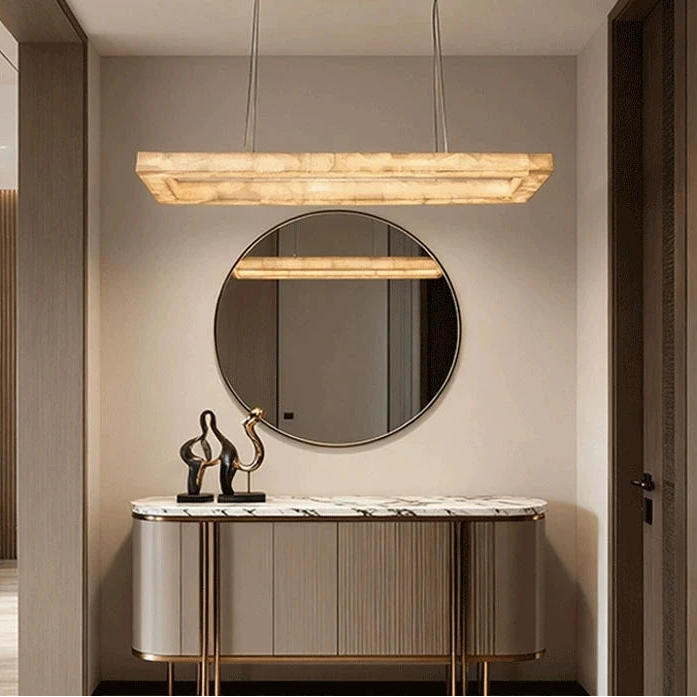 Alabaster linear chandelier with a gold canopy above a modern entryway console and round wall mirror