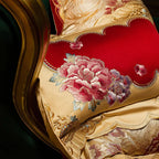 Red decorative pillow with dimensional pink peony embroidery, gold leaves, and ornate ivory edging – L&B