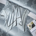 Folded light blue Egyptian cotton bedding with satin luster, layered shams, and detailed couture trim – L&B