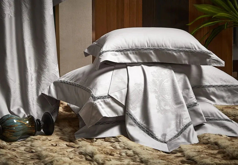 Silver gray damask bedding draped over an accent chair to display its jacquard pattern and flowing satin finish – L&B