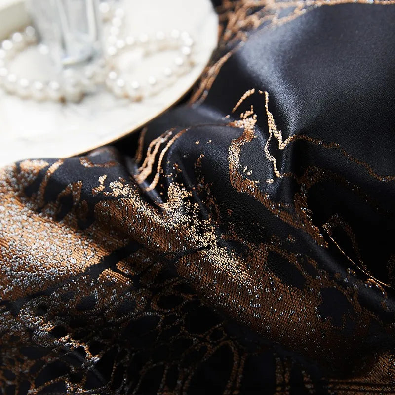 Close-up of black gold jacquard bedding with intricate copper scrollwork, luminous woven texture, and soft fabric folds – L&B
