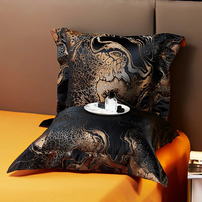 Black and gold jacquard pillow sham displayed with an ornate copper pattern and coordinating orange bedding – L&B