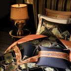 Luxury black bedding styled with gold medallion motifs and copper decorative pillows beside a table lamp – ROYAL H. BLACK – L&B