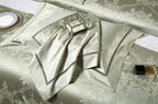 Folded sage green Egyptian cotton bedding with satin luster, couture-style bands, and detailed piping – L&B