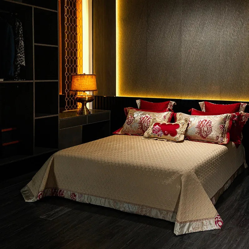 Thick quilted ivory bedspread styled with red floral embroidered pillows from the TROYAL bedding collection – L&B