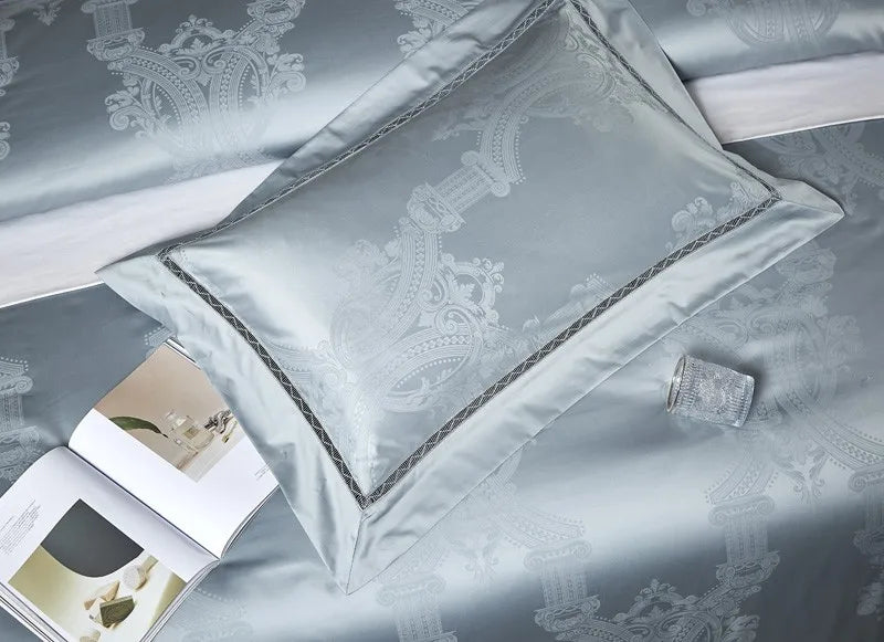 Light blue damask bedding with layered jacquard shams and tailored trim arranged on an elegant bed – L&B