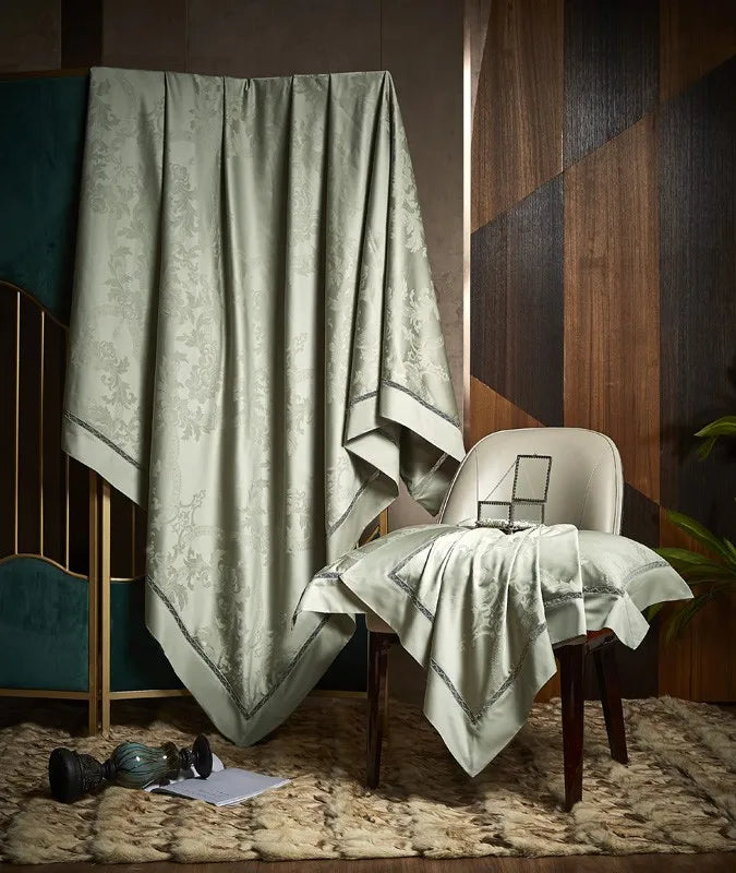 Sage green damask bedding draped over an accent chair to display its jacquard pattern and fluid satin finish – L&B