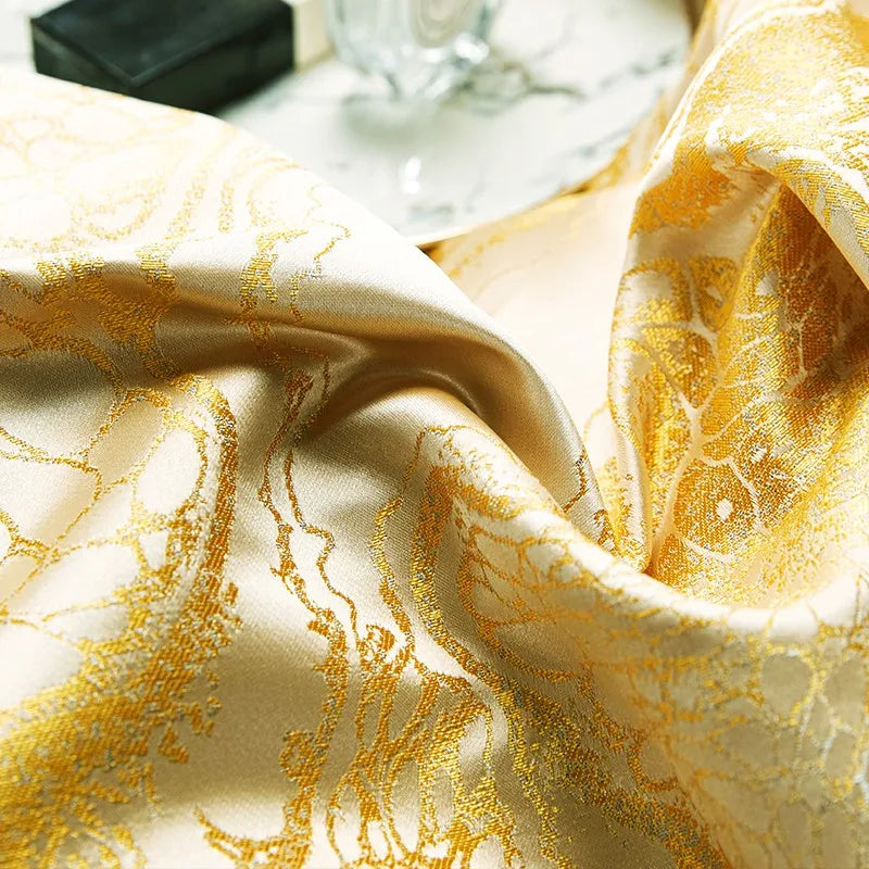 Macro view of gold jacquard bedding showing intricate woven scrollwork and luminous satin texture – L&B