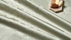 Close-up of smooth sage green Egyptian cotton satin fabric with a soft drape and subtle luminous sheen – L&B