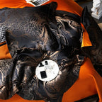 Close-up of luxury black jacquard bedding with copper-gold ornamental weaving and vivid orange accents – L&B