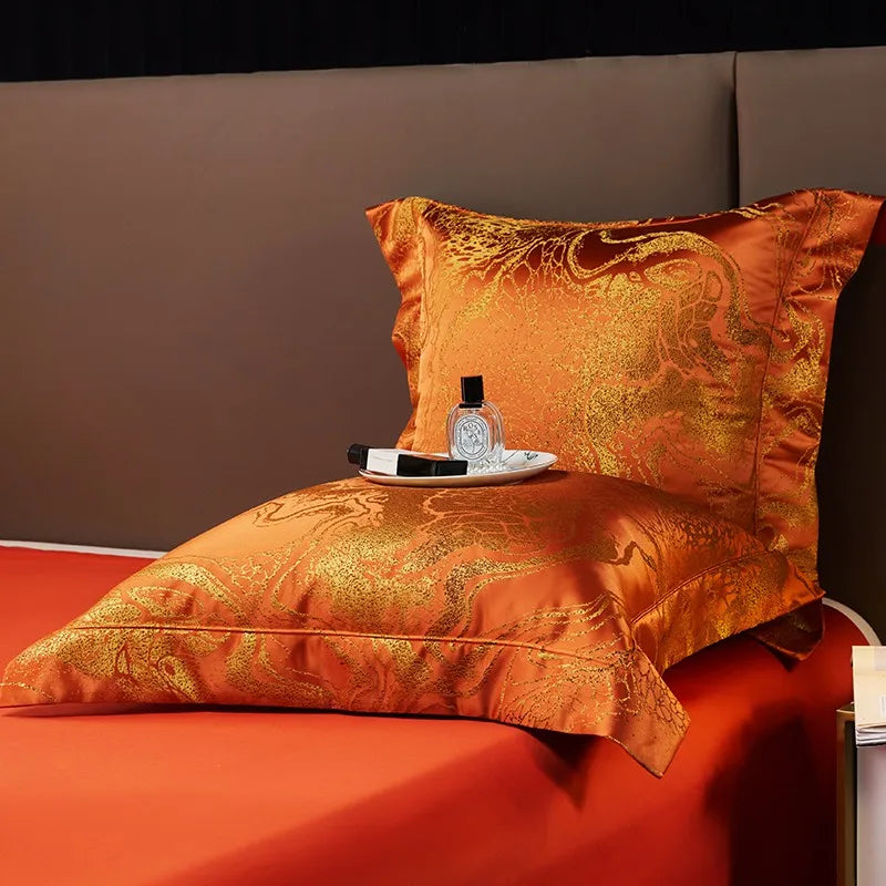 Ornate rust orange pillow sham and folded jacquard duvet cover displayed against a solid orange sheet – L&B