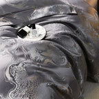 Close-up of charcoal gray jacquard bedding with flowing folds, platinum threadwork, and an intricate ornamental pattern – L&B