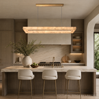 Alabaster linear chandelier with a gold canopy above a marble island in an organic modern kitchen with dark wood cabinets