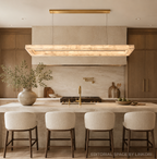 Large alabaster linear chandelier with a gold canopy over a marble kitchen island in a warm modern kitchen